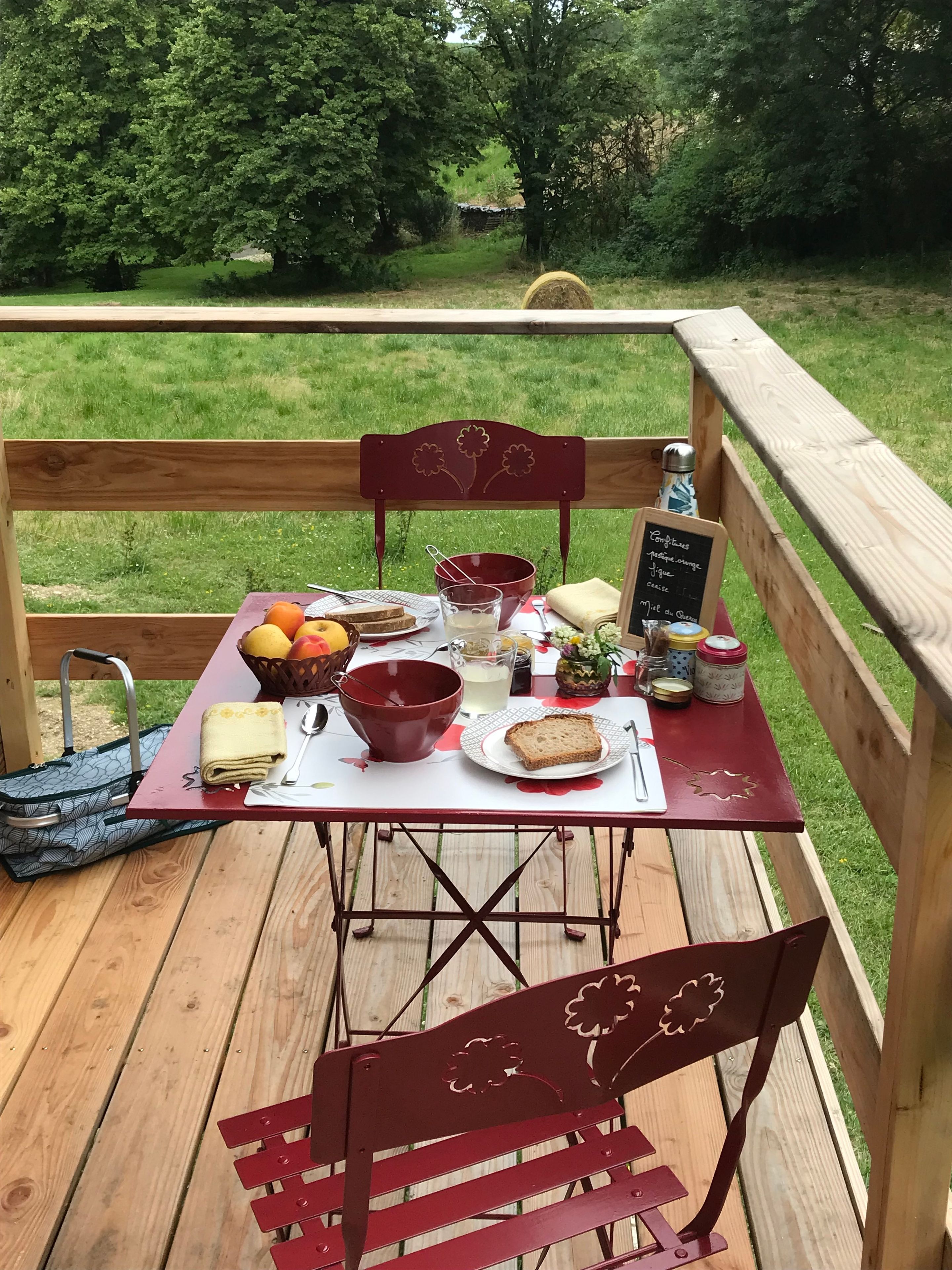 Een picknickopstelling op een houten terras, compleet met een tafel, stoelen en diverse soorten eten.