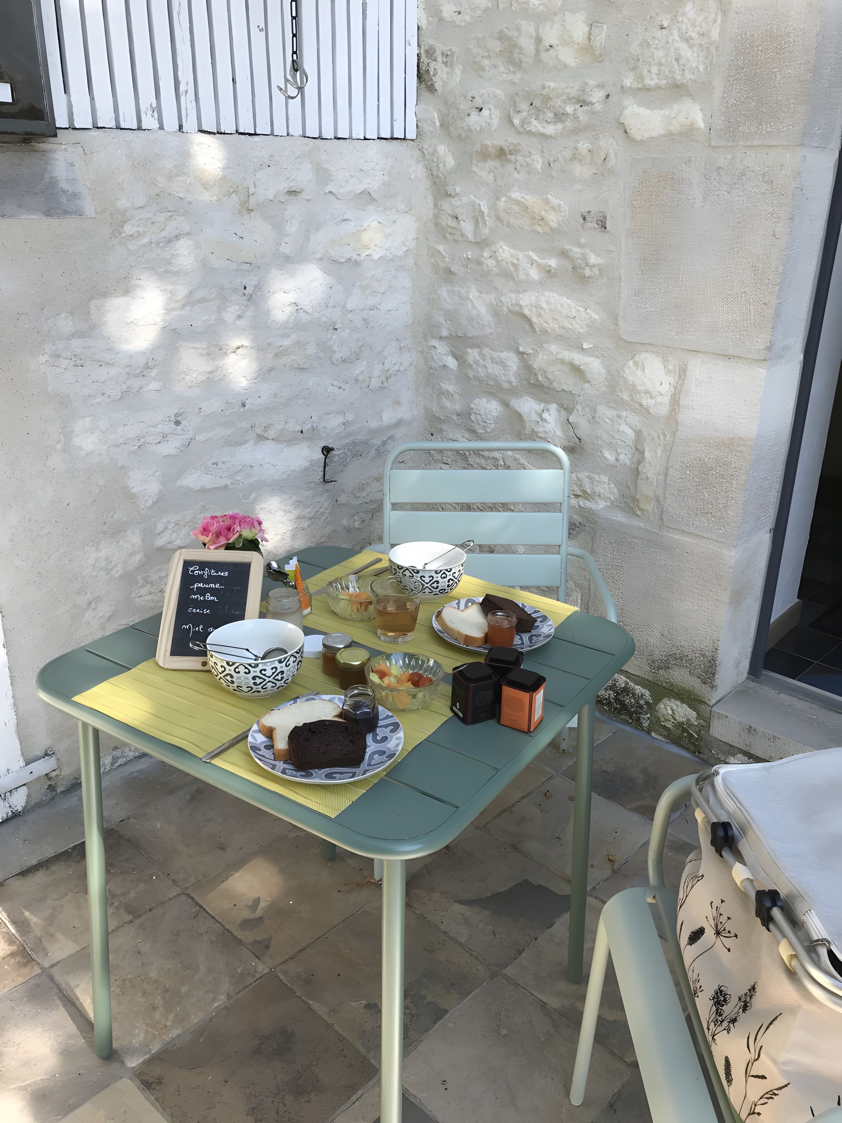 Une table dressée avec une variété de plats et un tableau noir servant de menu, le tout placé contre un mur de pierre.