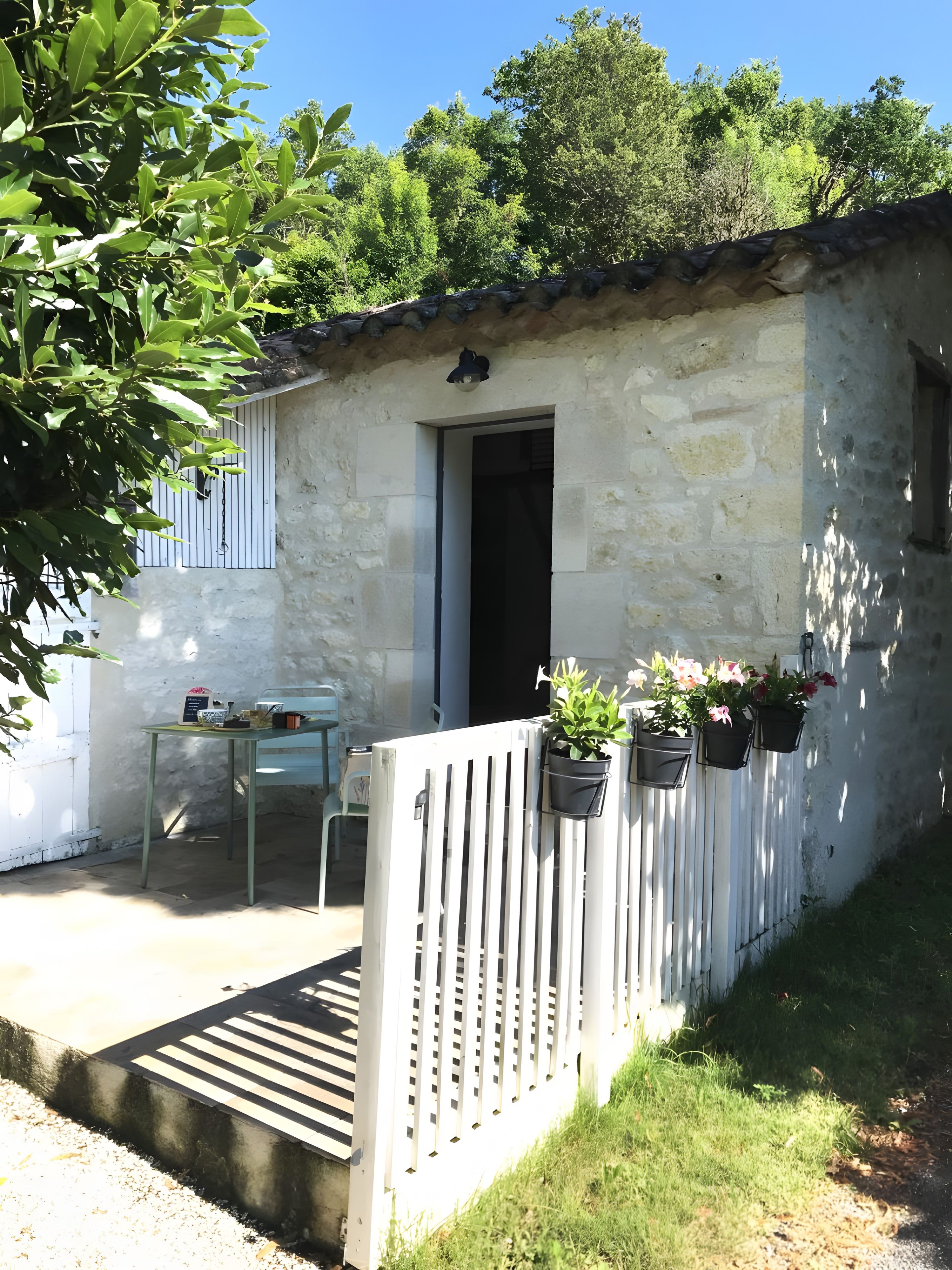 A rustic stone building with a door, a small table with items, and potted plants.