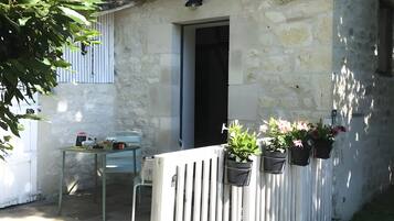 A rustic stone building with a door, a small table with items, and potted plants.