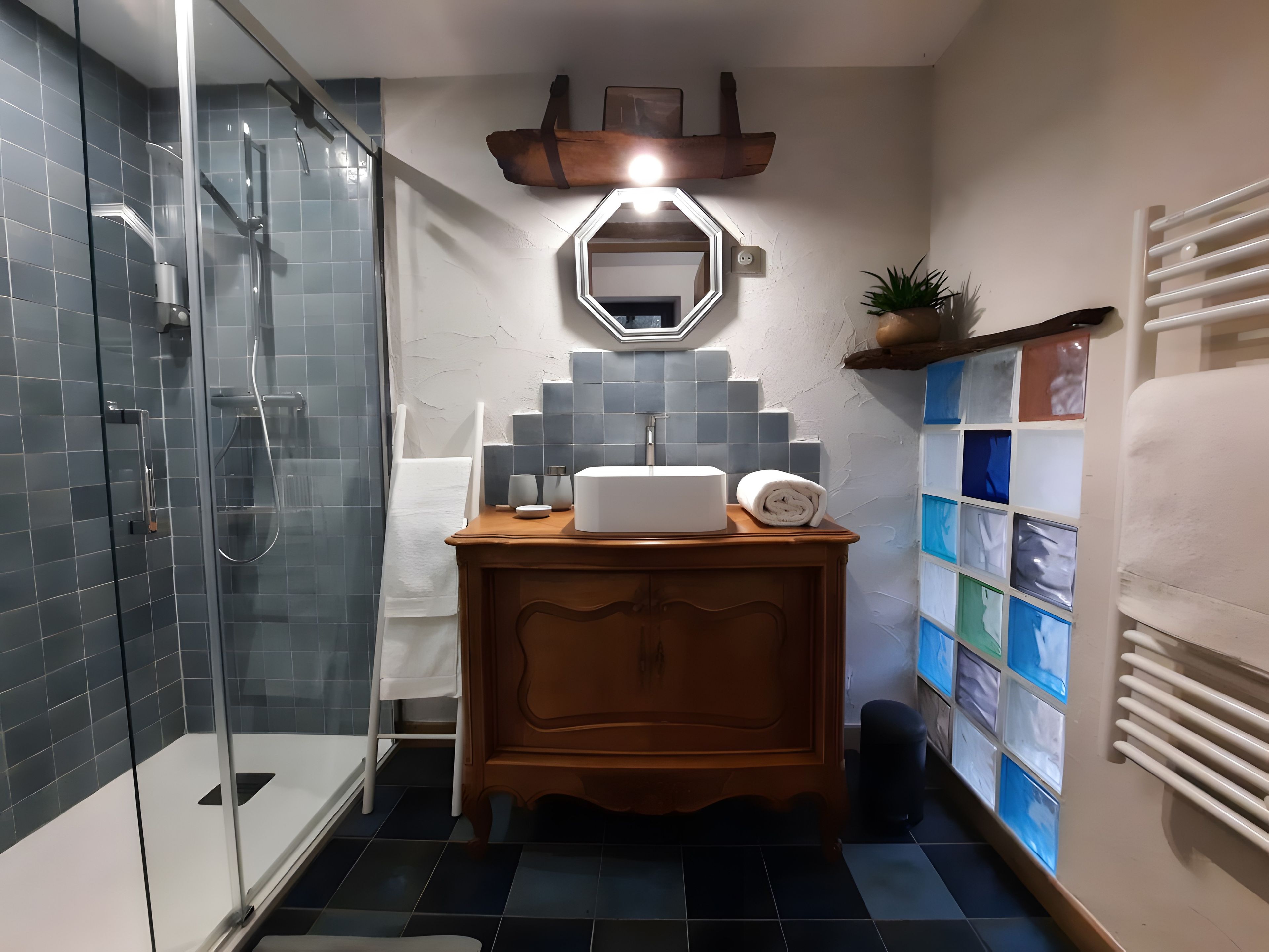 A bathroom with a glass shower enclosure, a wooden vanity with a mirror, and a wall-mounted towel rack.