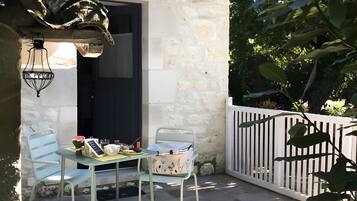 Een klein terras buiten met een tafel en twee stoelen, een stenen muur en een witte hek.
