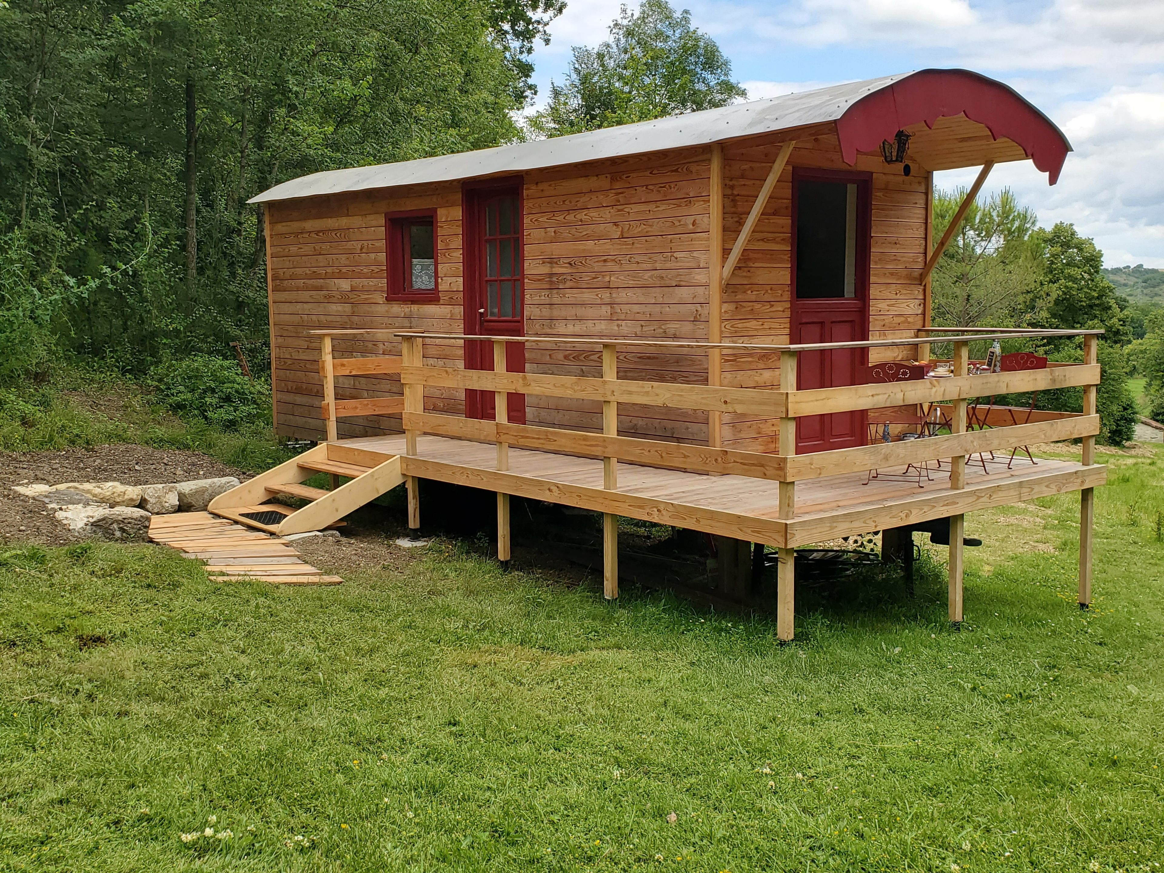 A wooden cabin with a wooden deck and a red door.