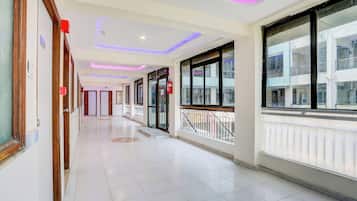 A hotel corridor with a tiled floor, wooden doors, and windows with a view of the outside.