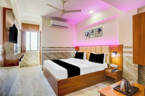 A hotel room with a bed, a nightstand, a coffee maker, a wall-mounted TV, and an air conditioning unit. - Townhouse Ambawadi Bus Terminal (Ahmedabad)