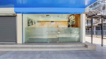 A building entrance with a blue awning, a closed shutter door, and a glass door with a security lock.