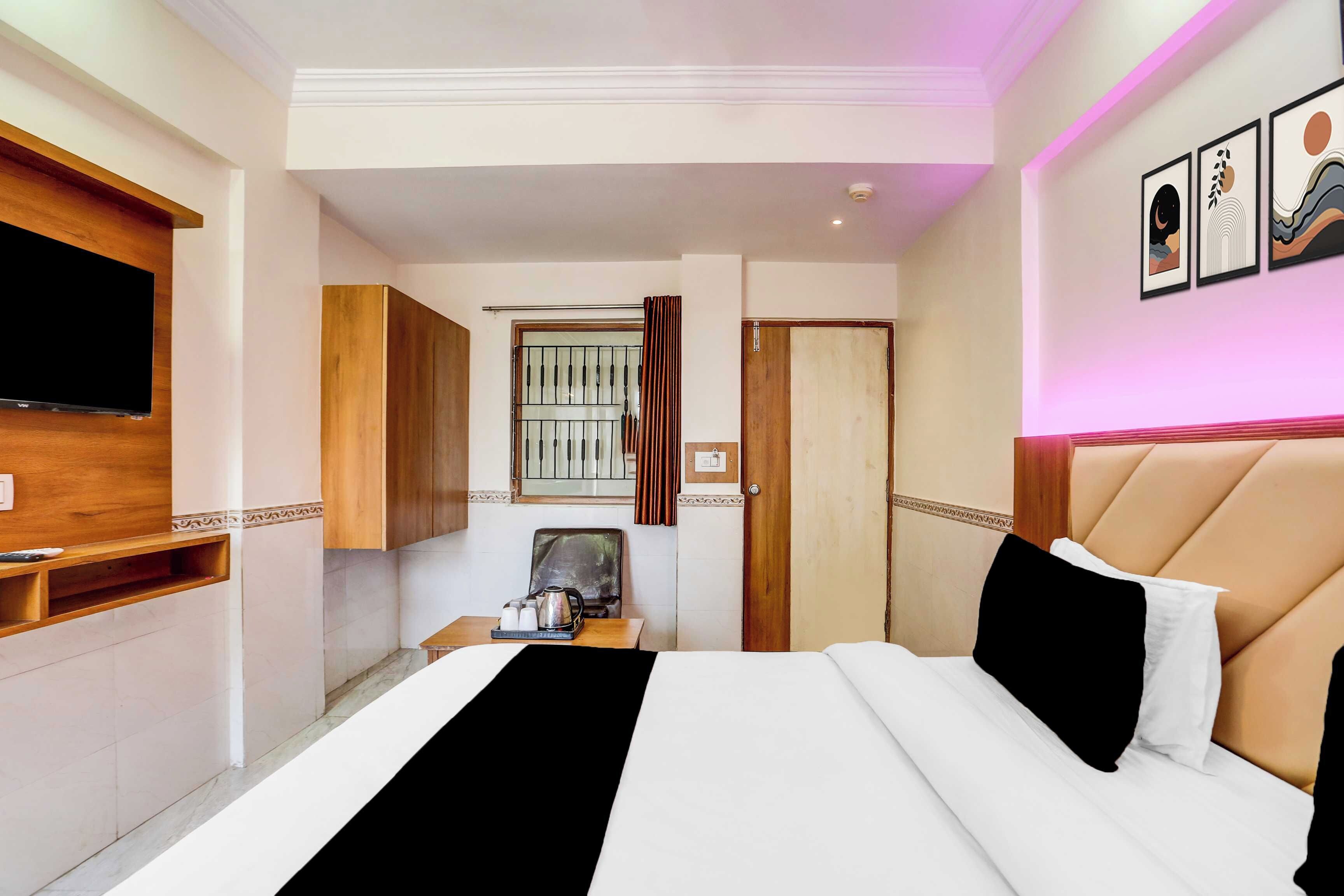 A hotel room with a bed, a TV, a desk with a chair, and a window with curtains.