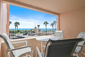 A balcony with a view of a parking area, palm trees, and a building with a flagpole. - Jetty East 117a (Destin)