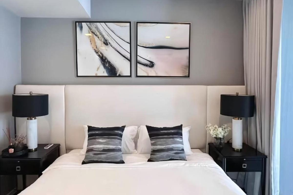A hotel room with a bed, two nightstands, a lamp on each, and two abstract paintings on the wall.