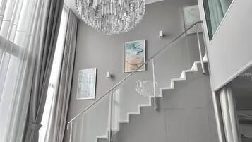 A modern interior with a staircase, a chandelier, and a dining area with chairs and a table.