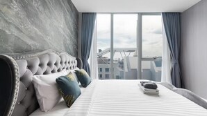Une chambre à coucher moderne avec une tête de lit capitonnée, une grande fenêtre avec des rideaux et une vue sur la ville.