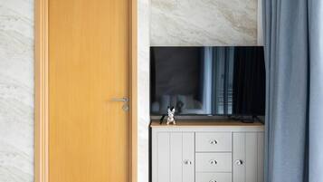 A room with a wooden door, a white cabinet with drawers, and a television on a marble wall.