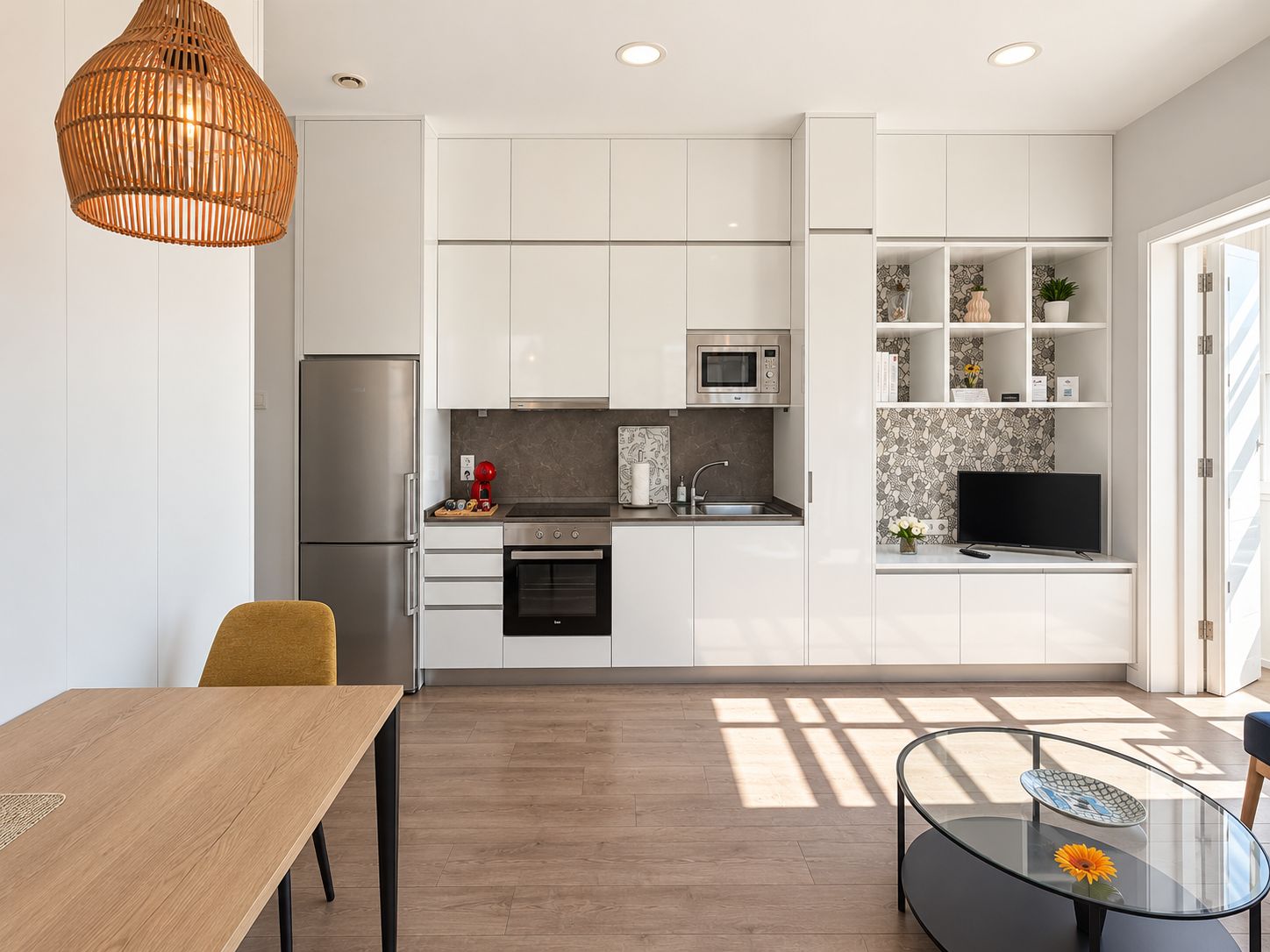 A modern kitchen with white cabinetry, a built-in microwave, and a dining area with a wooden table and chairs.