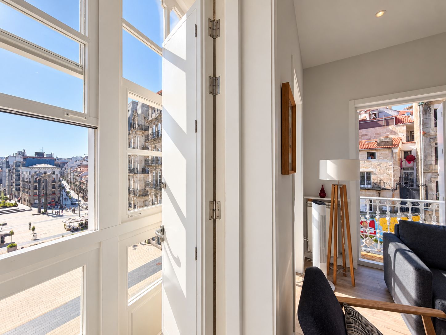 Una habitación con ventanas amplias, vistas a un paisaje urbano, un balcón con barandilla y un sofá.