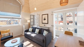 A modern living room with a sofa, a glass coffee table, a wooden dining table, and a view of the city through large windows. - Apartamentos Abrente - Porta Do Sol (Vigo)