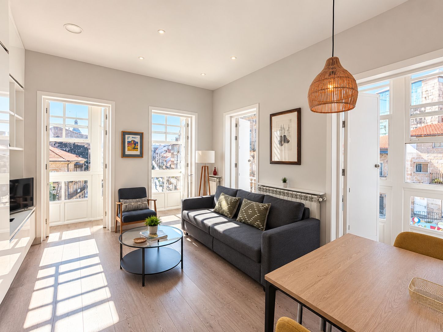 Un salon spacieux comprenant un canapé, une table basse et une table à manger. De nombreuses fenêtres offrent une vue sur la ville.