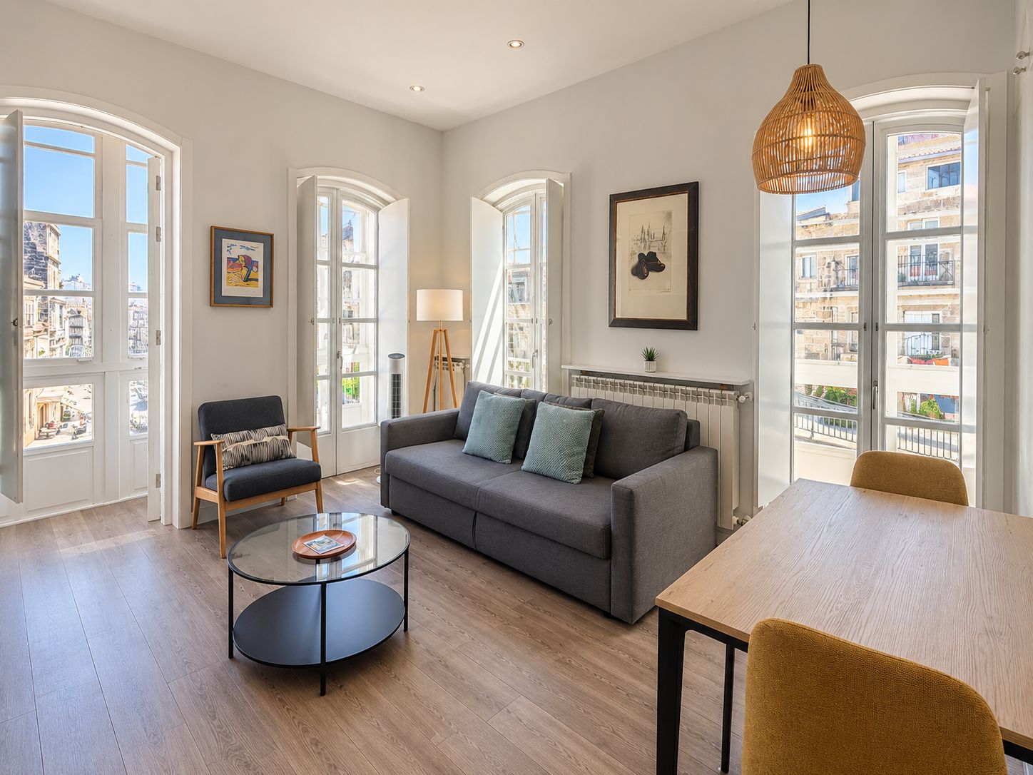A spacious living room with a grey sofa, a round coffee table, and a wooden dining table.