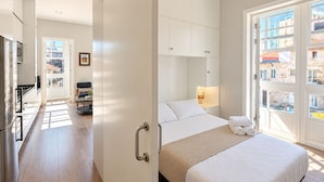 A modern hotel room with a bed, bedside table, and a view of the city through large windows. - Apartamentos Abrente - Porta Do Sol (Vigo)