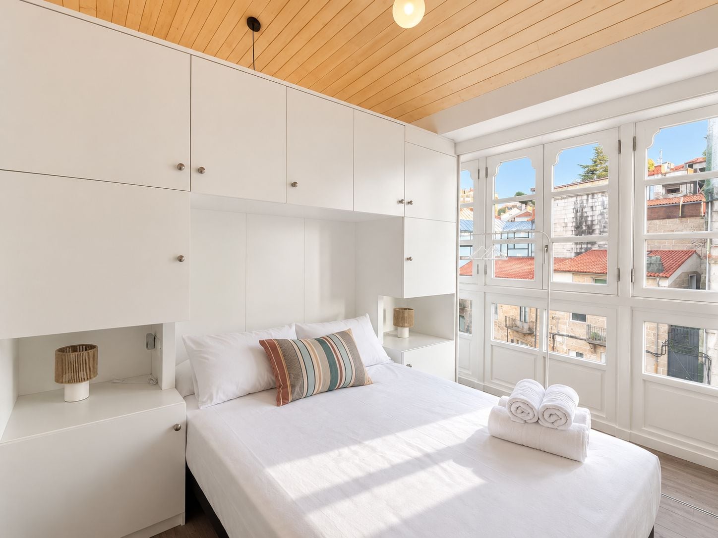 A bedroom with a large bed, white cabinets, and a view of buildings through the window.