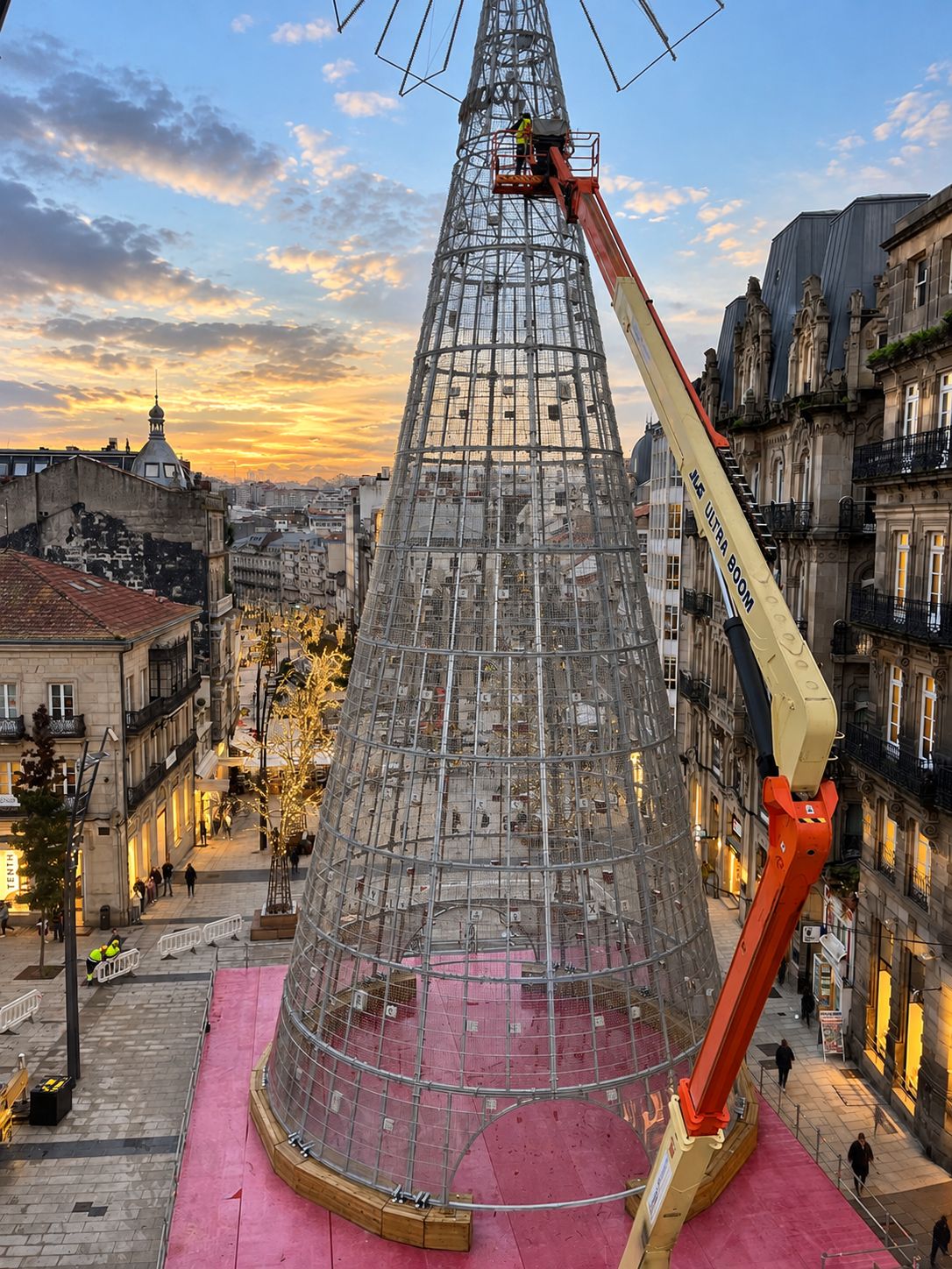 A large, transparent, conical structure with a crane positioned on its side, set against a backdrop of historic buildings and a sunset sky.