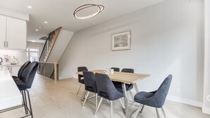 Uma sala de jantar com mesa de madeira e cadeiras modernas, uma escada e um quadro na parede.