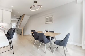 Et spiseområde med et træbord, moderne stole, en trappe og et billede i ramme på væggen.