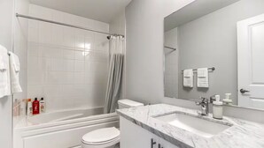 Uma casa de banho moderna com banheira, sanita e um espelho grande.