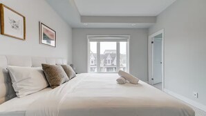 Quarto com uma cama grande, janela com vista para edifícios e uma porta.