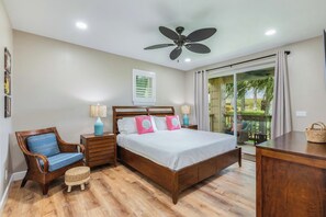 A bedroom with a bed, wooden nightstands, a chair, a ceiling fan, and a view of the outdoors. - Pili Mai 15F - newly remodeled (Poipu)