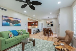 A spacious living room with a green sofa, a coffee table, and a dining area with wooden chairs and a table. - Pili Mai 15F - newly remodeled (Poipu)