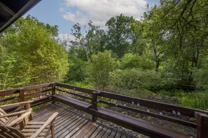 Une terrasse en bois avec des bancs donnant sur une zone boisée.