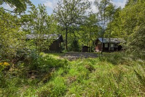 A rustic cabin with a gravel driveway, surrounded by dense greenery and trees. - Strae Cabin a Wooden Cabin in the Dalavich Countryside (Dalavich)