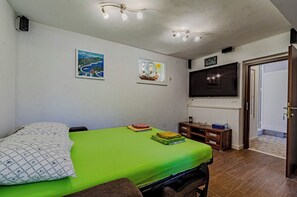 Un dormitorio con una colcha verde, un televisor de pantalla plana grande montado en la pared y un pequeño mueble de madera.