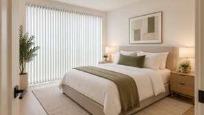 A bedroom with a bed, bedside tables, a lamp, a plant, and a window with blinds. - Toren Hotel & Suites (Toronto)