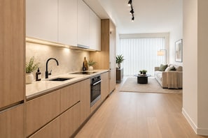 Una cuina moderna amb armaris de fusta, forn integrat i un rentaplat. Hi ha una zona de menjador amb un sofà i una taula de centre.