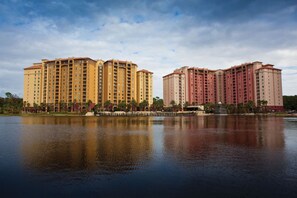 A large hotel complex with multiple high-rise buildings, a body of water in the foreground, and a clear sky. - Orlando | Pool & Disney Access | 2BR Suite (Lake Buena Vista)