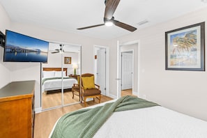 Habitación de hotel con cama, una silla, televisor, ventilador de techo y un cuadro en la pared.