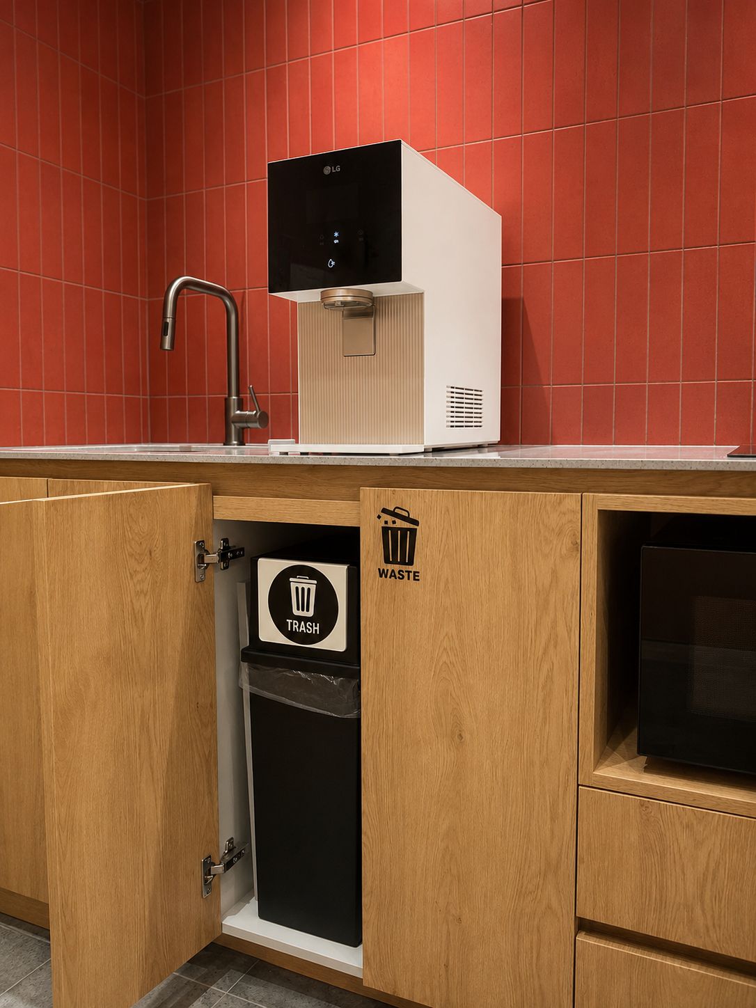 A kitchen with a red tiled backsplash, a sink, a trash bin, and a microwave.