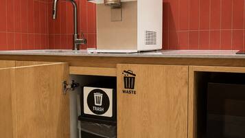 A kitchen with a red tiled backsplash, a sink, a trash bin, and a microwave.