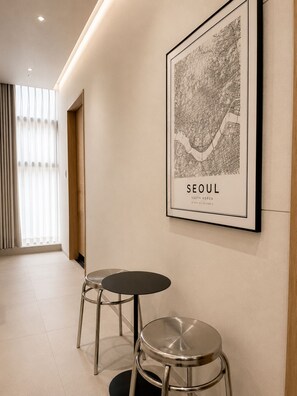 A hallway with a framed map of Seoul, two metal stools, and a door with blinds.