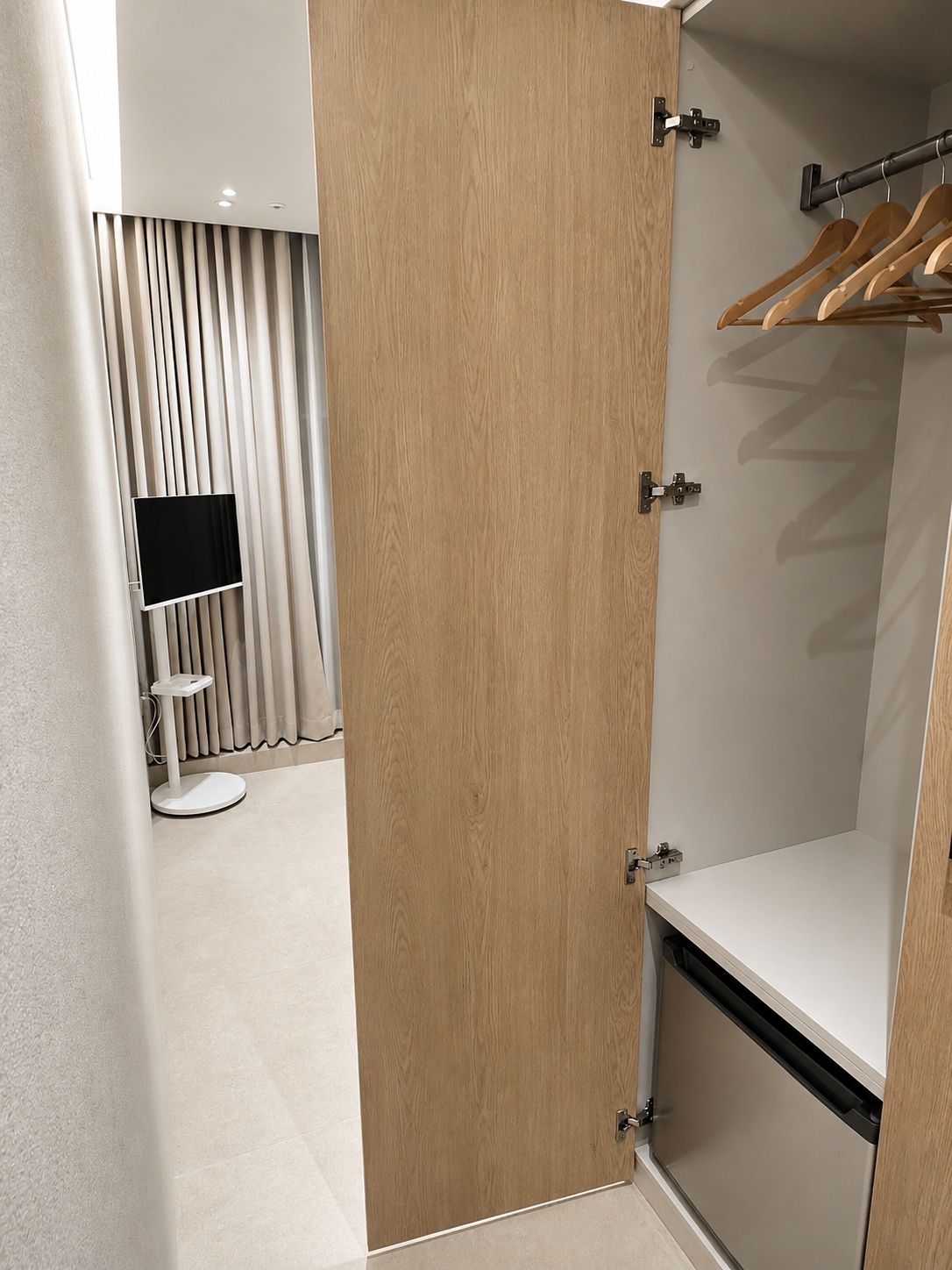 Een hotelkamer met een houten garderobe, een televisie en een kledingrek.
