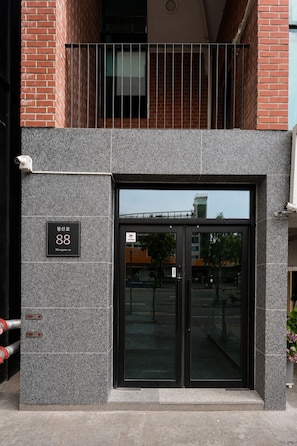 Entrada d'un edifici amb una porta de vidre, una reixa de metall i un senyal que indica l'adreça.