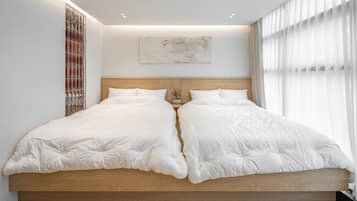 A double bed with a wooden headboard, a wall-mounted abstract painting, and a window with sheer curtains.
