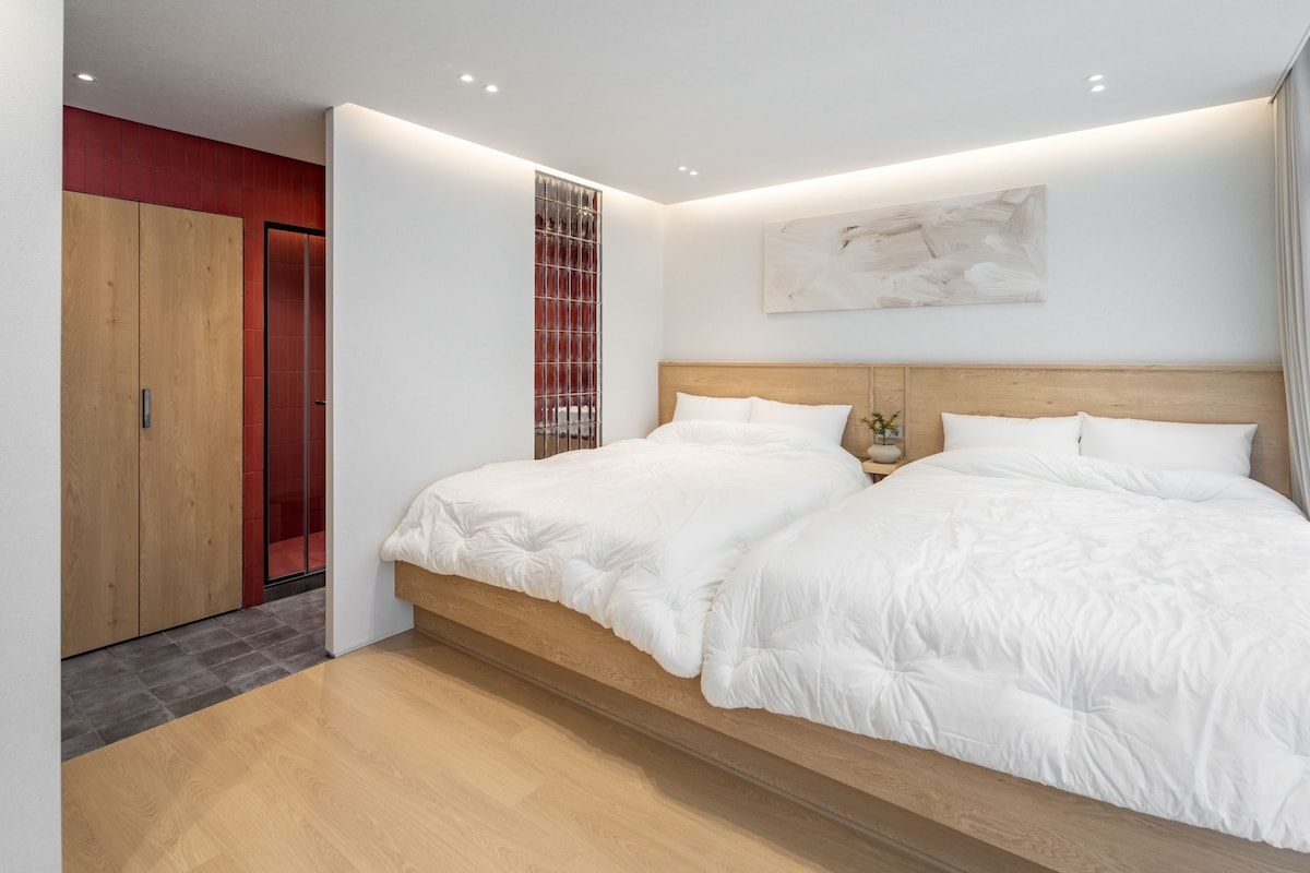 Une chambre moderne avec un grand lit, une tête de lit en bois et un mur d’accent rouge.