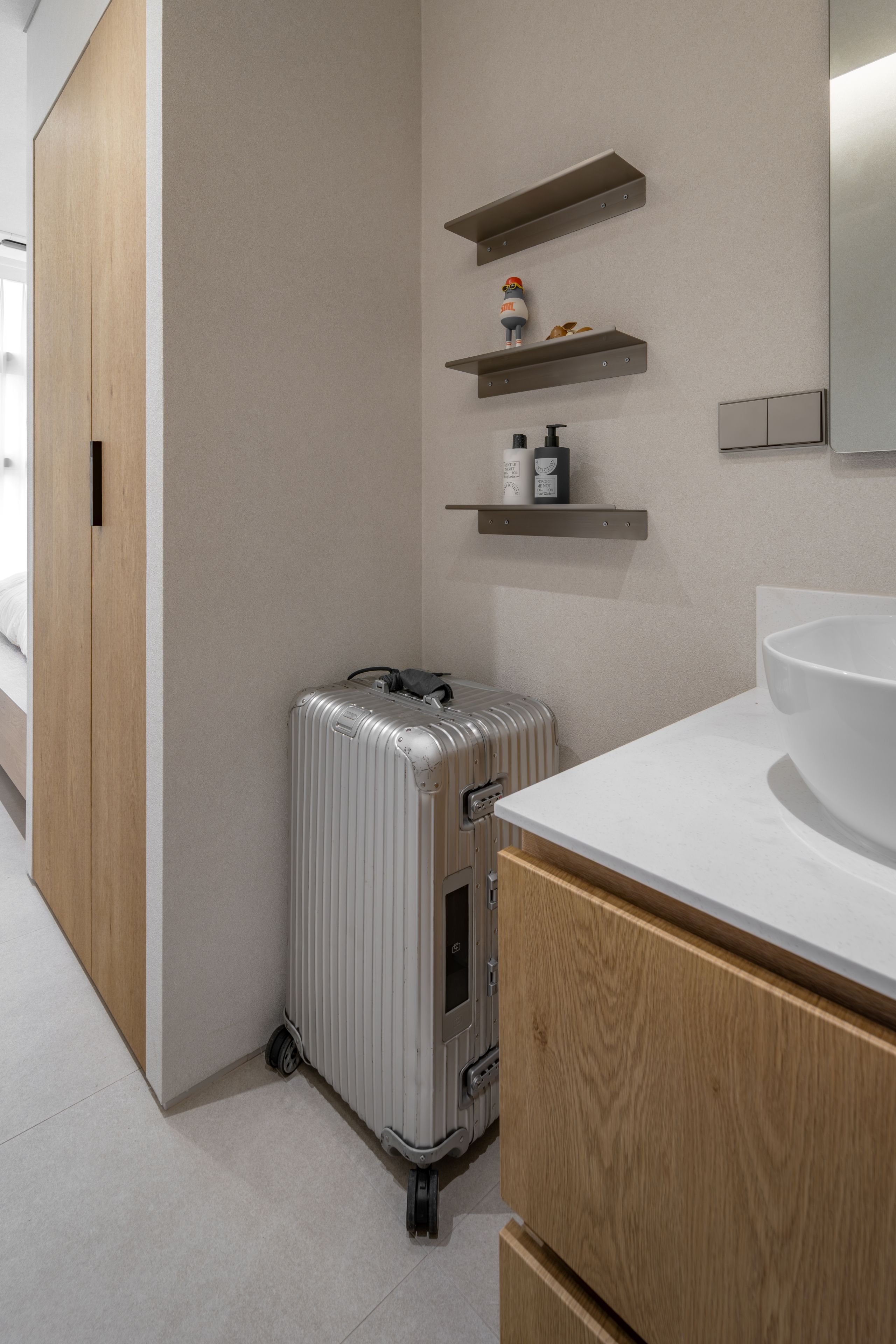 A modern bathroom with a large sink, a suitcase, and wooden cabinets.
