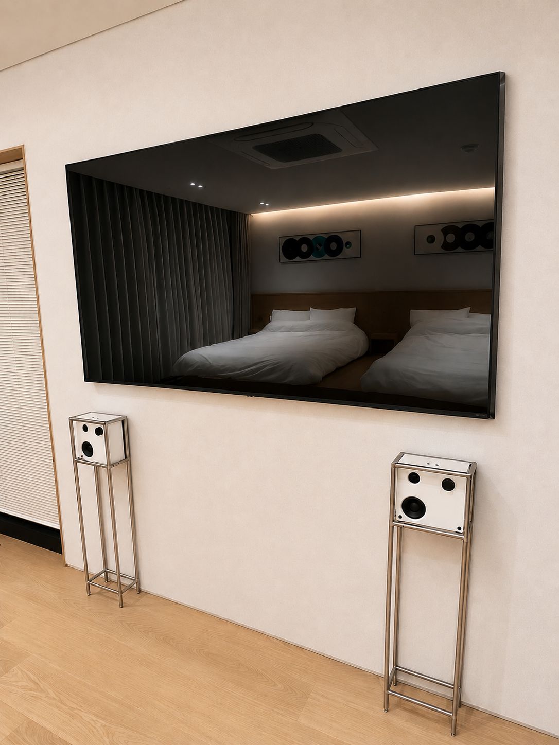 A modern hotel room with a large wall-mounted TV, two bedside tables, and a bed with white bedding.