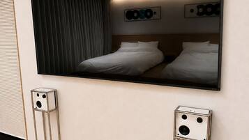 A modern hotel room with a large wall-mounted TV, two bedside tables, and a bed with white bedding.