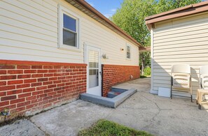 A single-story house with a brick foundation and siding, a front door, and a small porch area with two chairs.