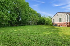 A grassy backyard with a house, trees, and a clear sky.