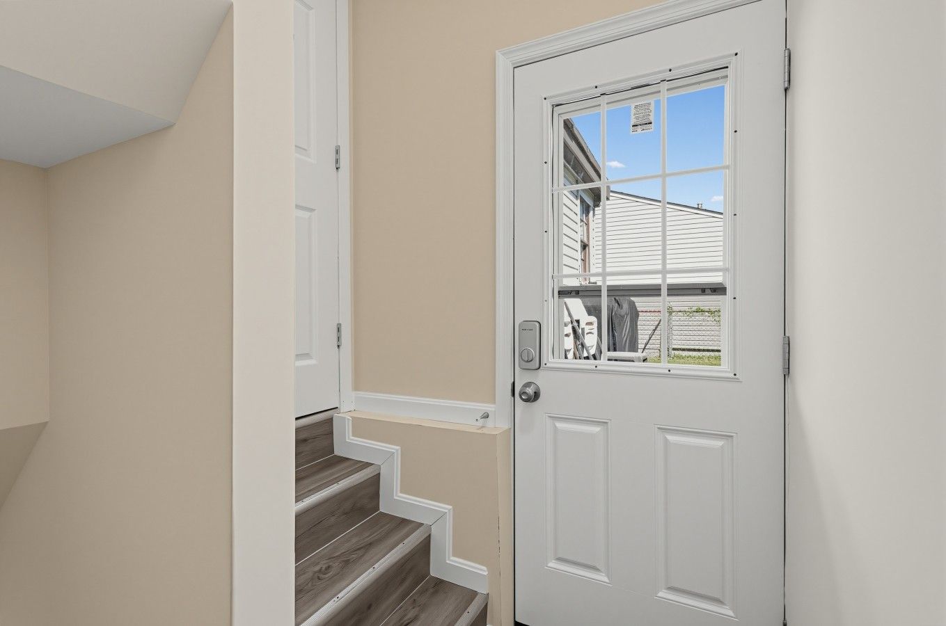 A white door with a window, a wooden staircase, and beige walls.